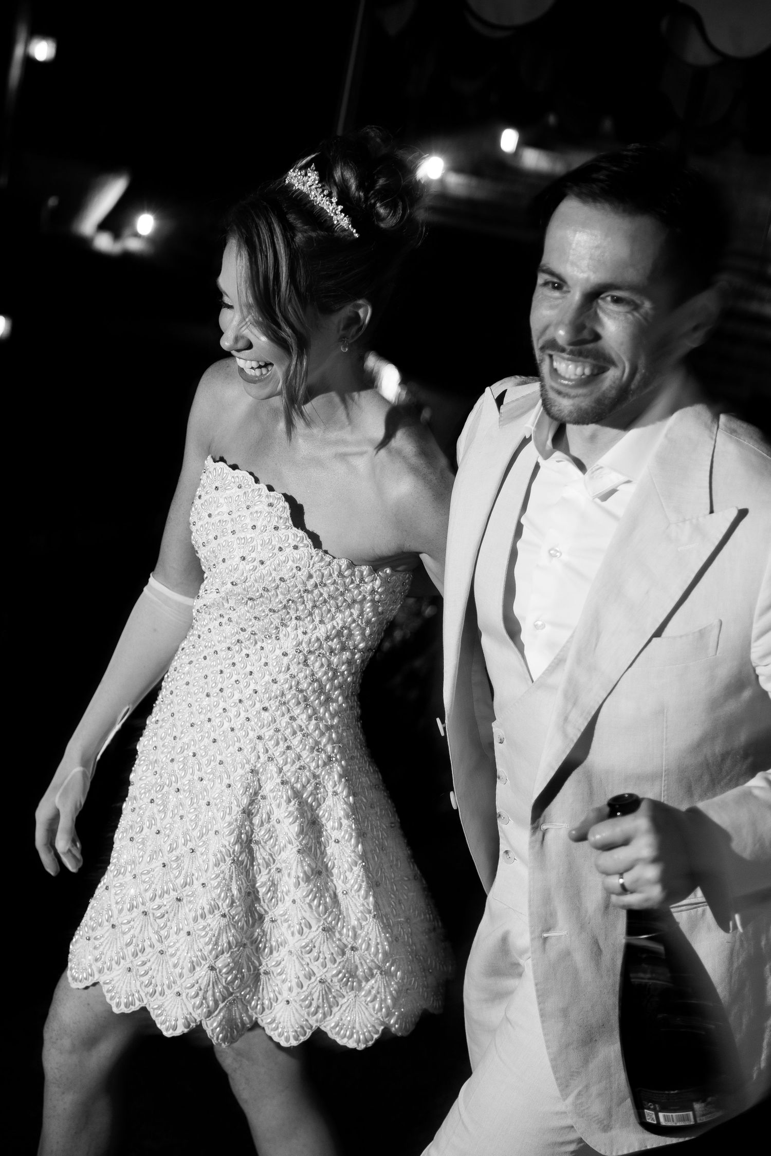 Black and white photo of laughing bride and groom dancing together at their wedding reception.