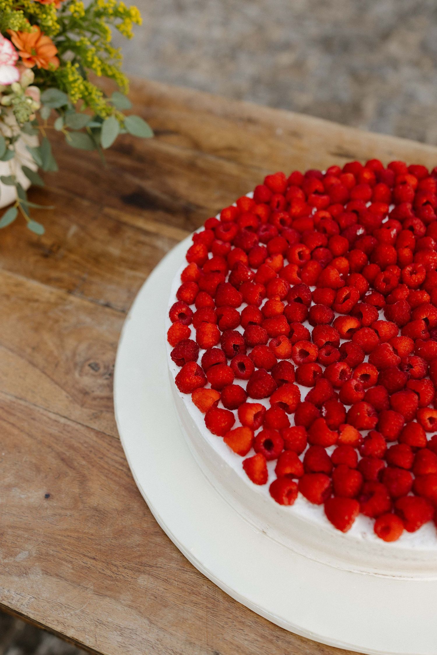 Elegant white wedding cake topped with fresh red raspberries and strawberries on a rustic wood table.