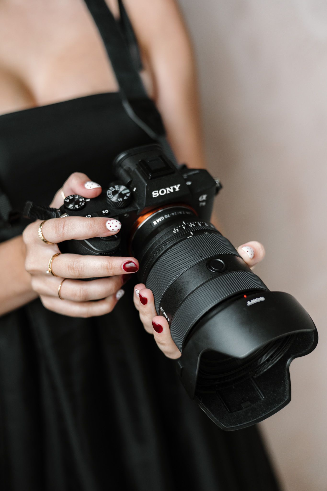Woman in black dress holding a Sony mirrorless camera with large lens, red manicured nails visible.