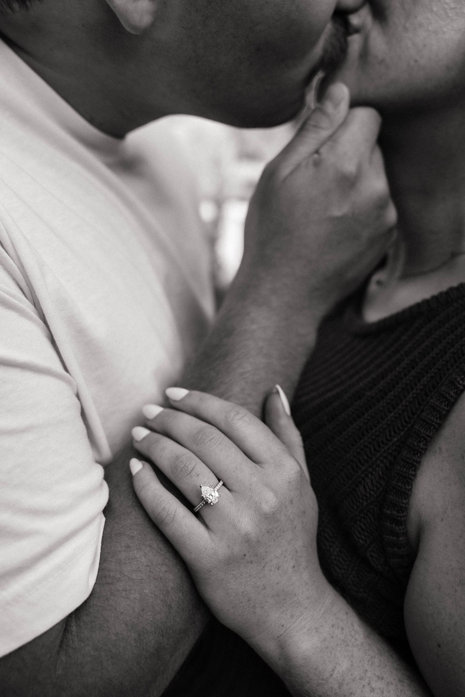 Black and white photo of a couple kissing, showcasing a sparkling diamond engagement ring on the woman's hand.