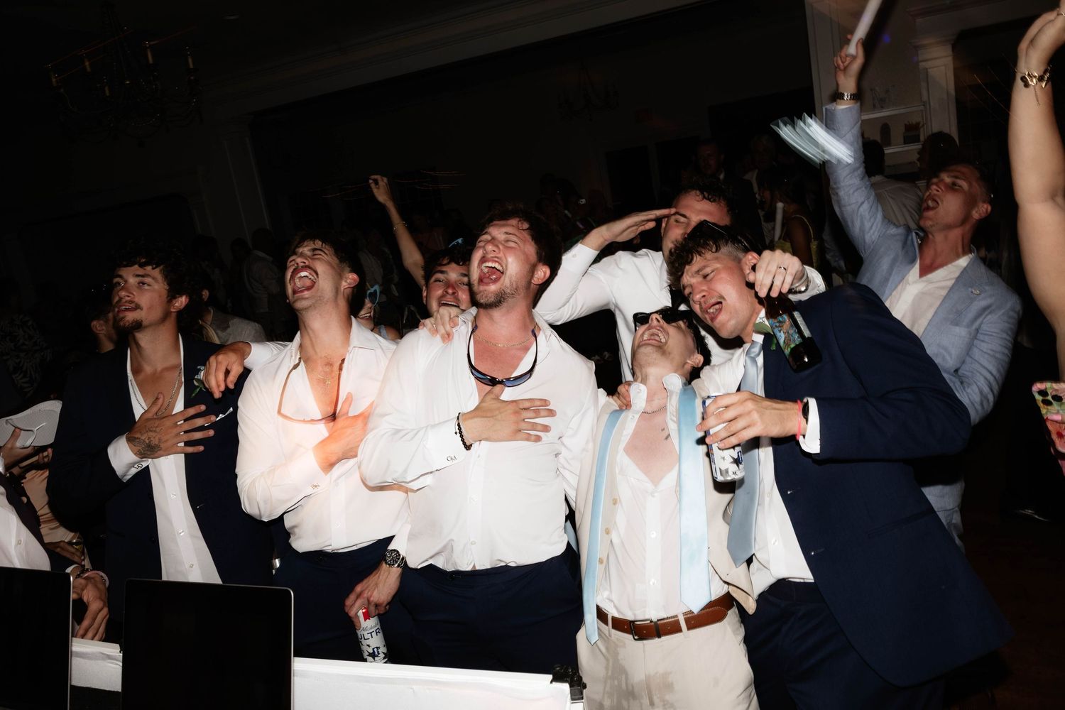 Men in white shirts and suits celebrating joyfully at a wedding reception party.