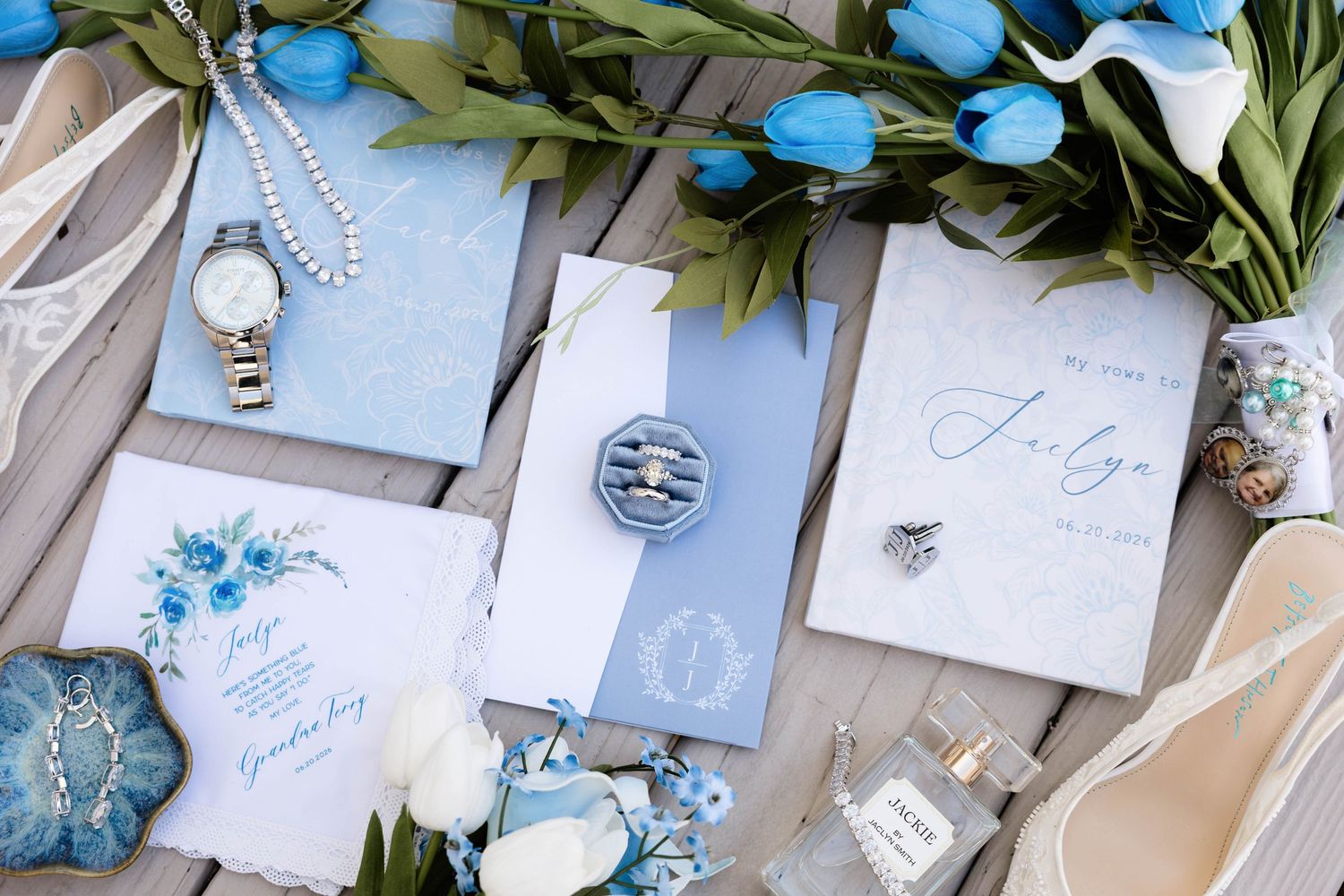 Blue and white wedding stationery flatlay with tulips, ring, perfume, and elegant accessories on wooden surface.
