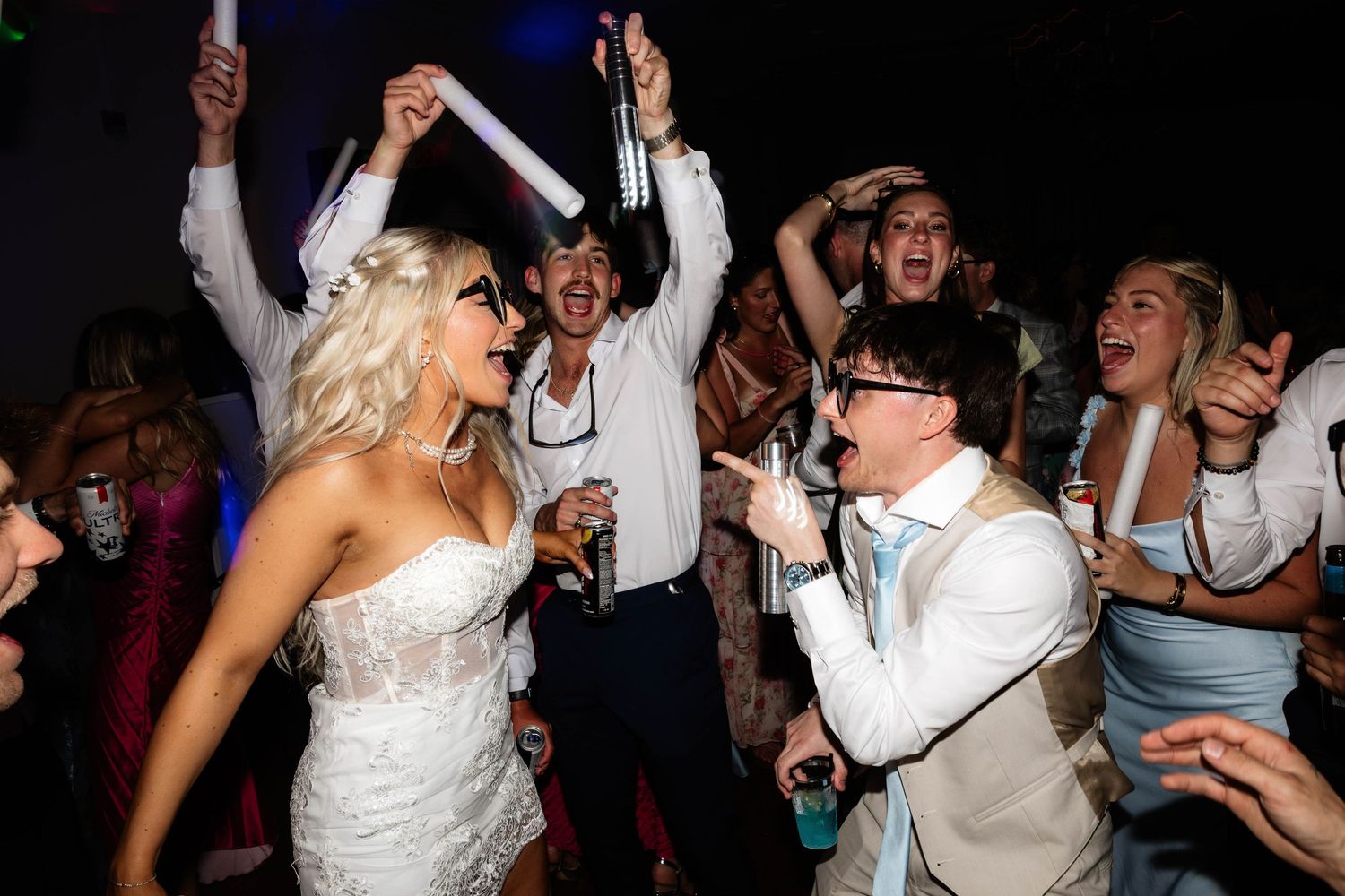 Bride and groom celebrate joyfully on the dance floor surrounded by cheering wedding guests at a lively reception.