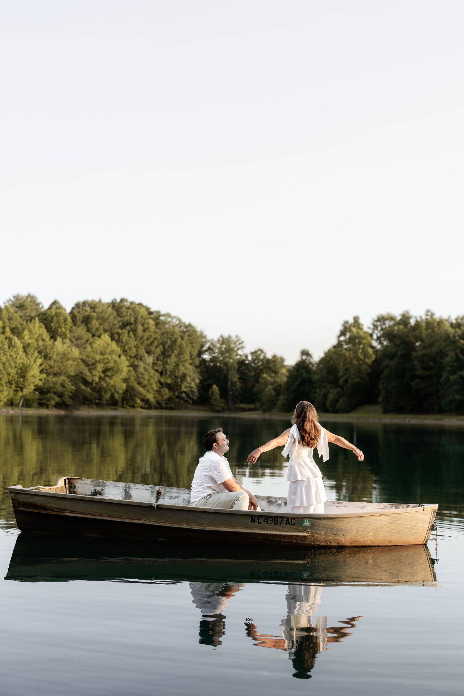 Couple sharing a romantic moment on a wooden rowboat on a calm lake surrounded by lush green trees.