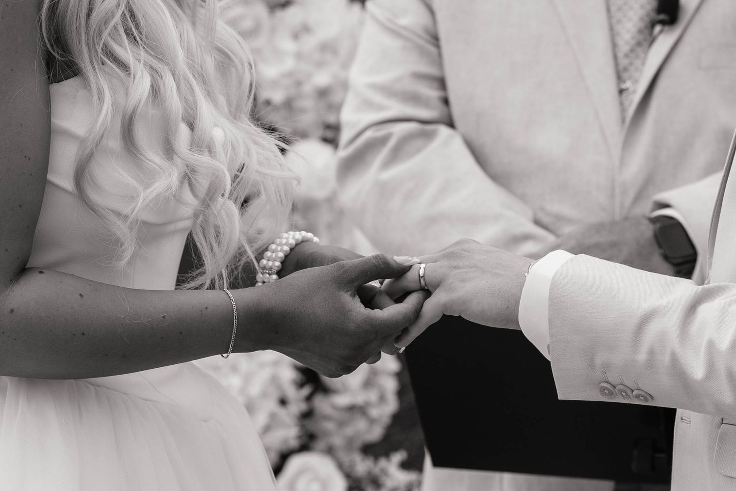 Black and white photo of bride and groom exchanging wedding rings during ceremony.