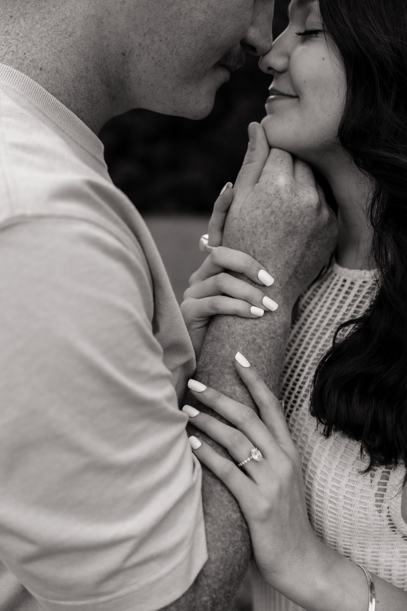 Black and white photo of a couple about to kiss, hands tenderly touching, engagement ring visible.