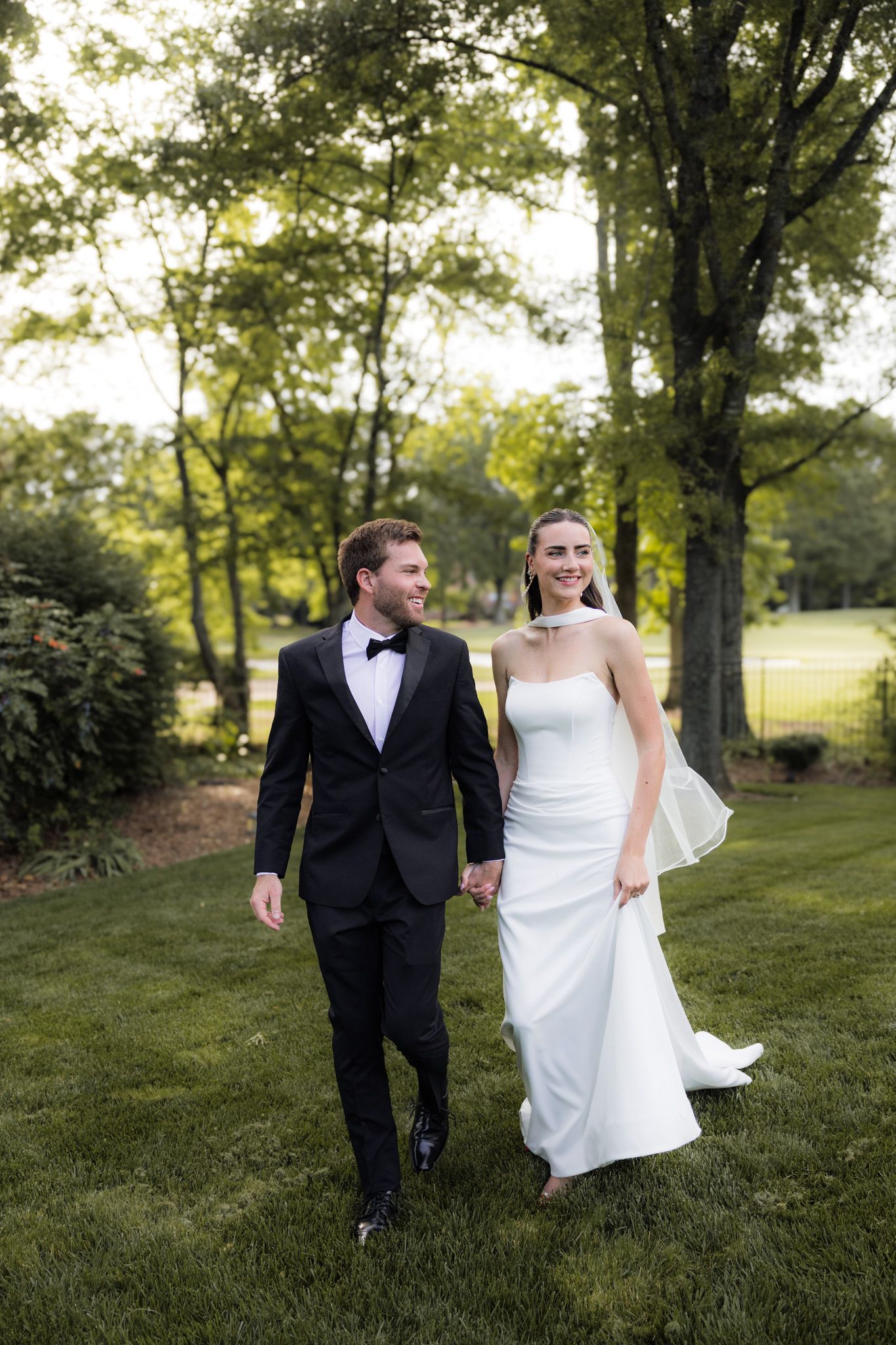 Newlywed couple walking together on grassy lawn during outdoor wedding photoshoot.