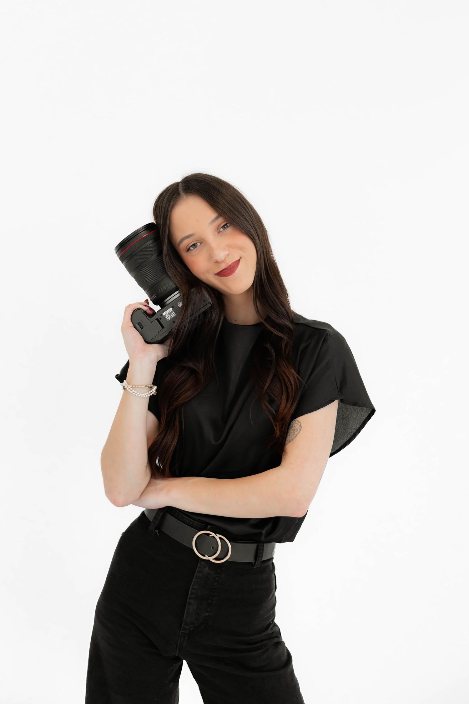 Professional photographer in all black outfit holding camera against white background.