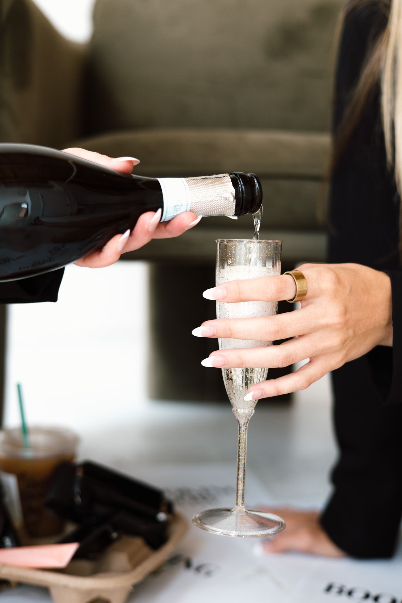 A woman holding a champagne flute while someone pours sparkling wine from a dark bottle at a celebration.