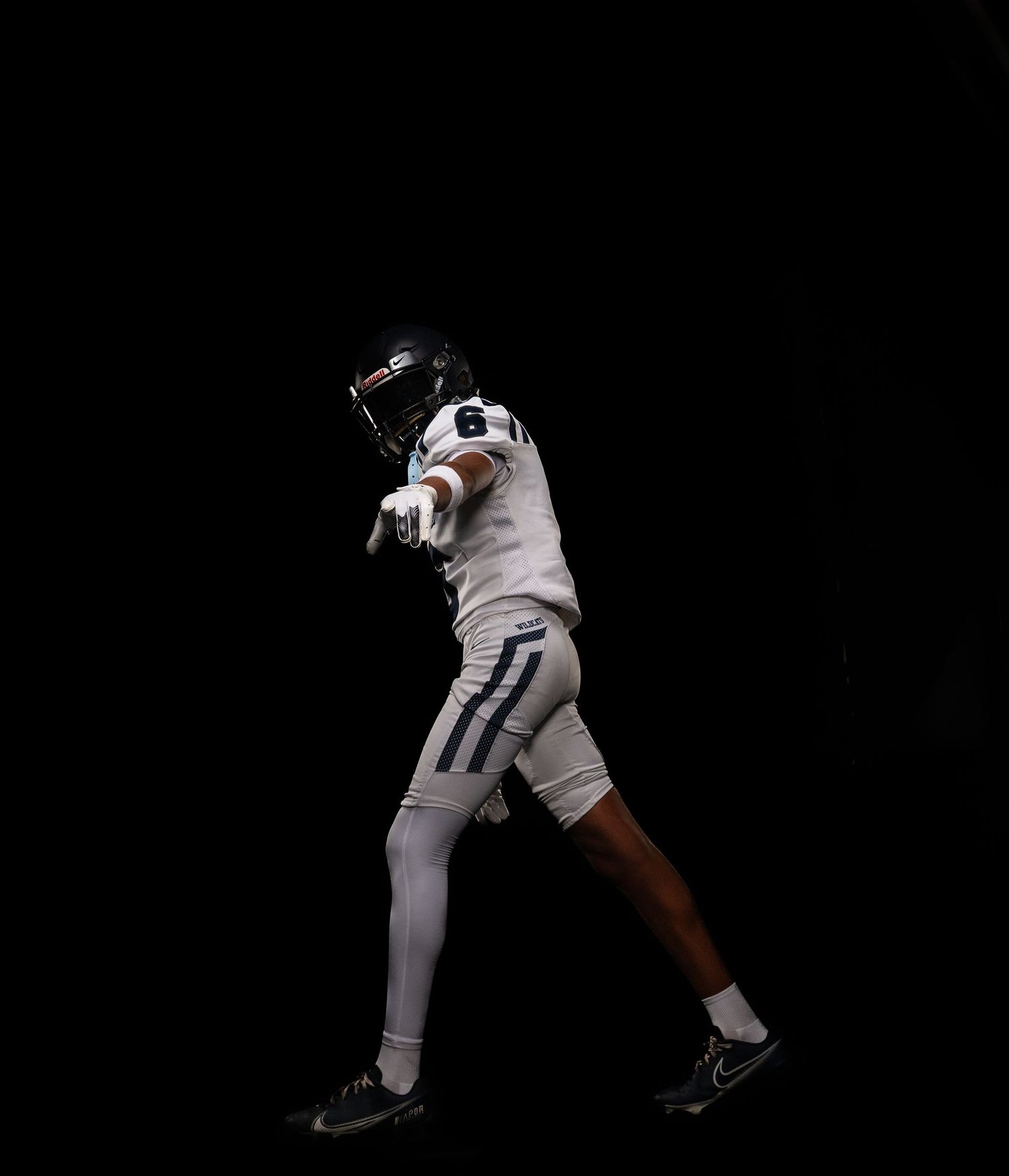 Football player in white uniform points forward dramatically against a black background.