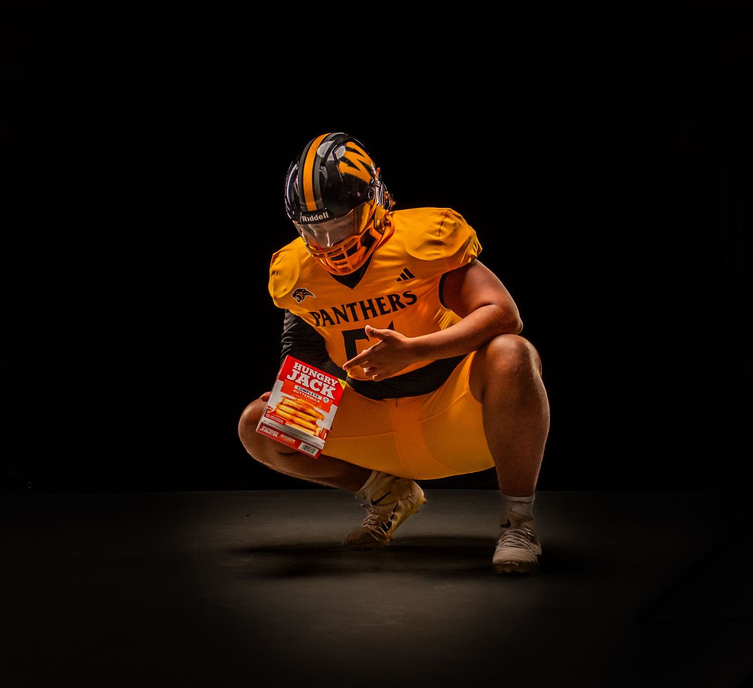 Football player in gold Panthers uniform crouching dramatically against dark background holding a book.