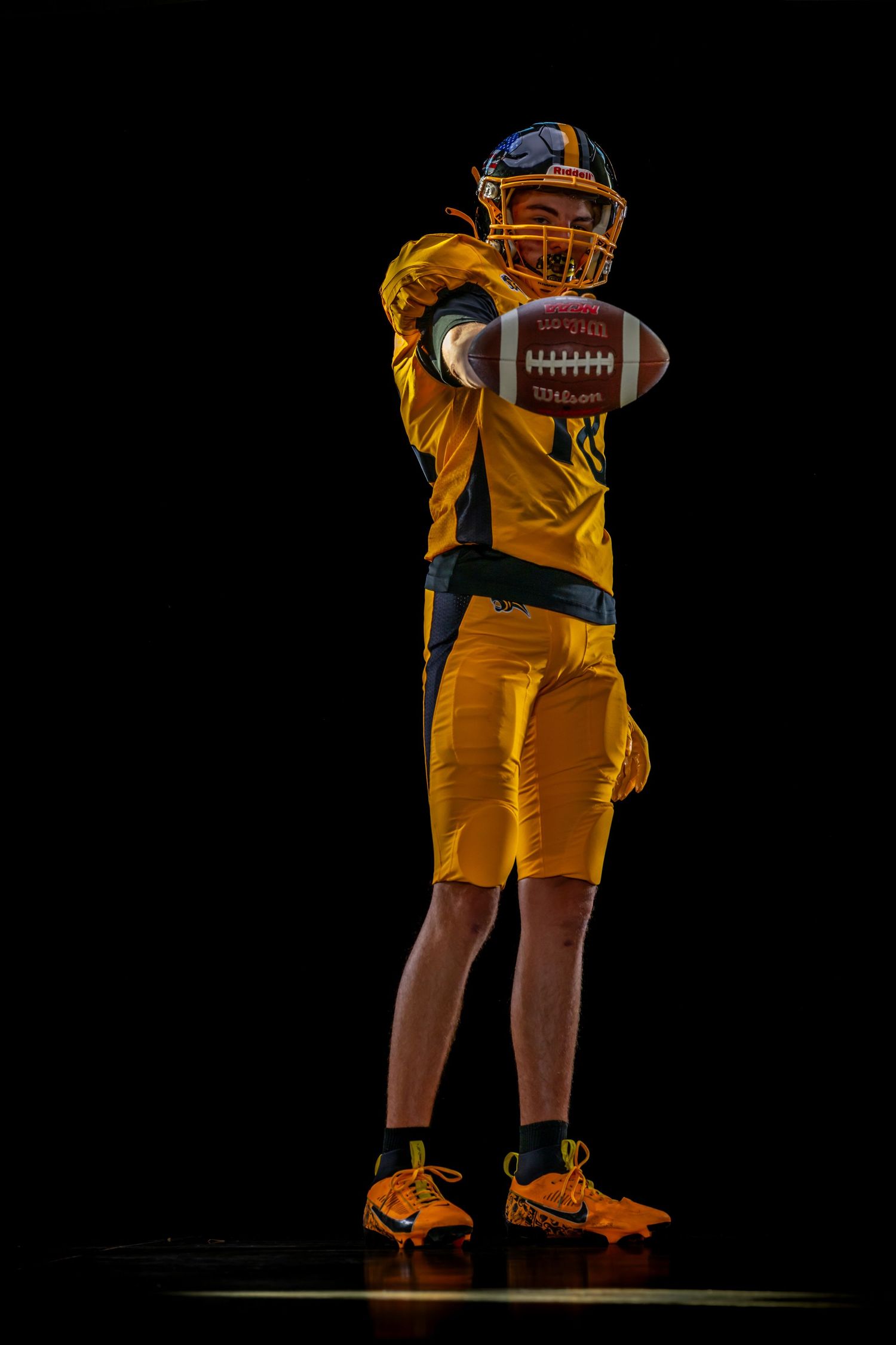 American football player in yellow uniform holding a football against a dark background.