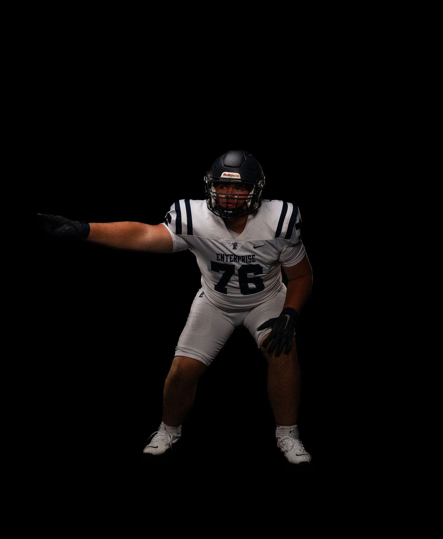 Football player number 76 in white Enterprise uniform points outward against solid black background.