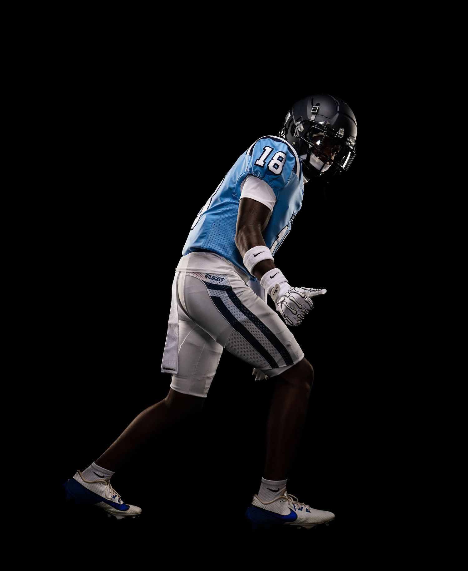 Football player in light blue jersey number 16 with white pants poses dynamically against a black background.