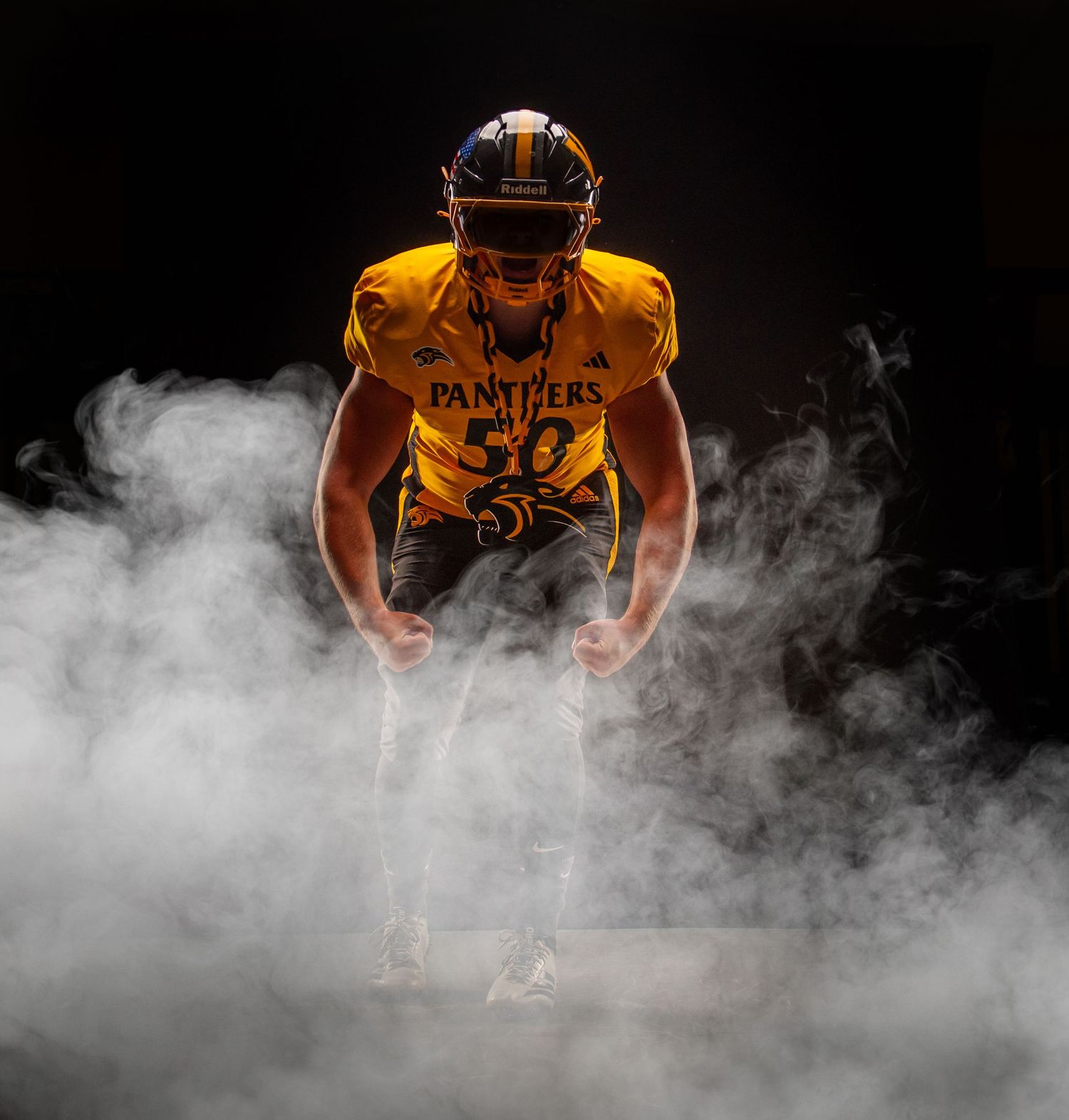 Panthers football player #50 in gold uniform emerges dramatically through smoke in dark stadium lighting.