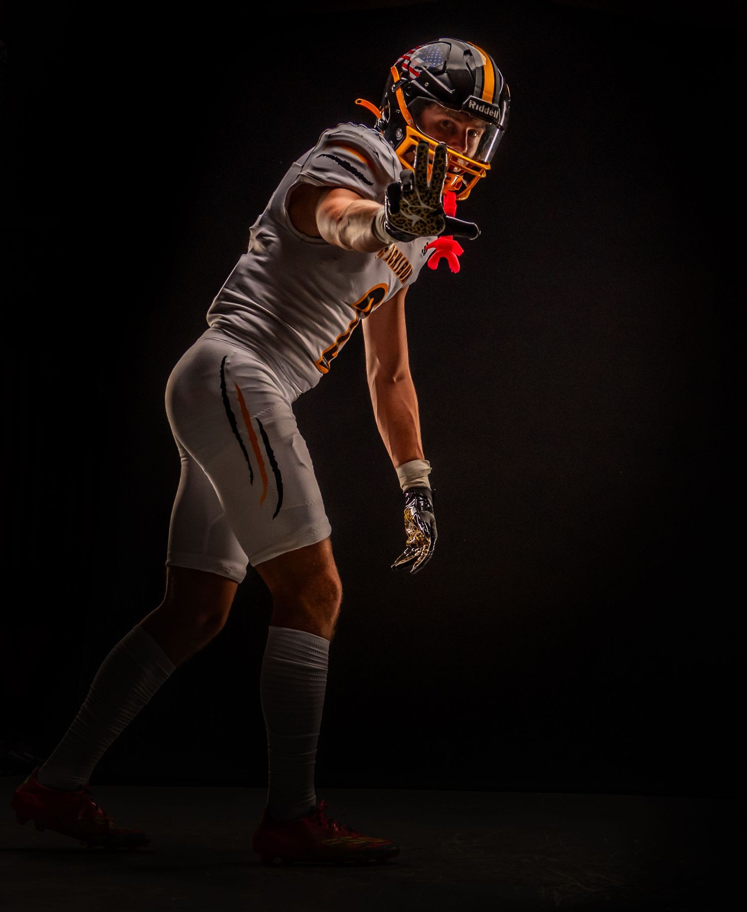 American football player in white uniform and orange helmet posing in dramatic dark studio lighting.