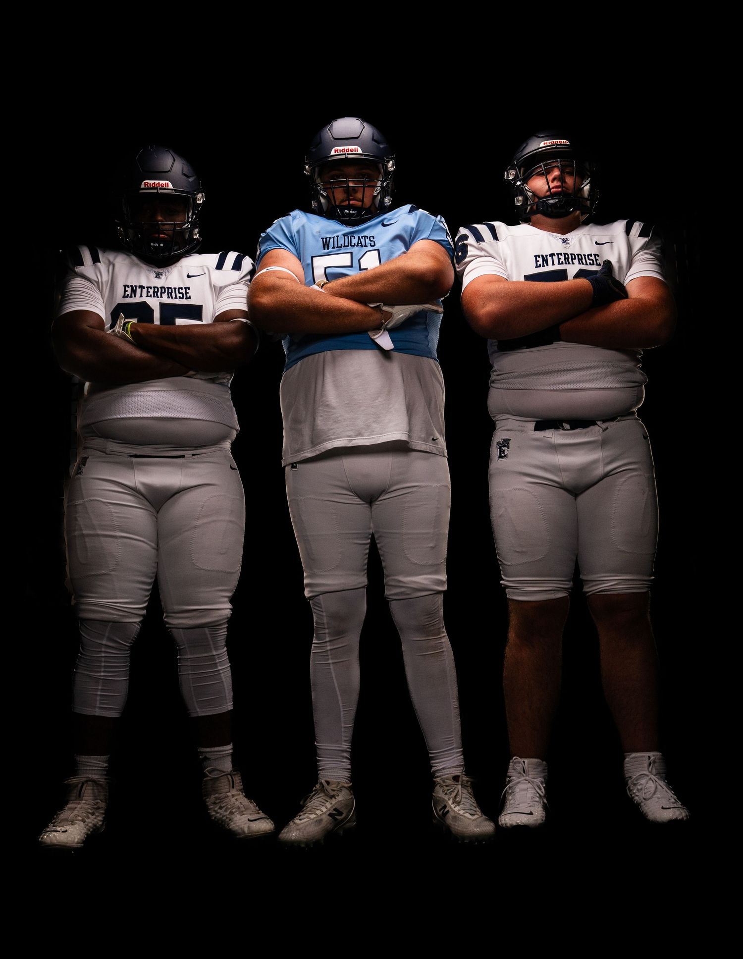 Three football players in Enterprise and Wildcats uniforms stand arms crossed against black background.