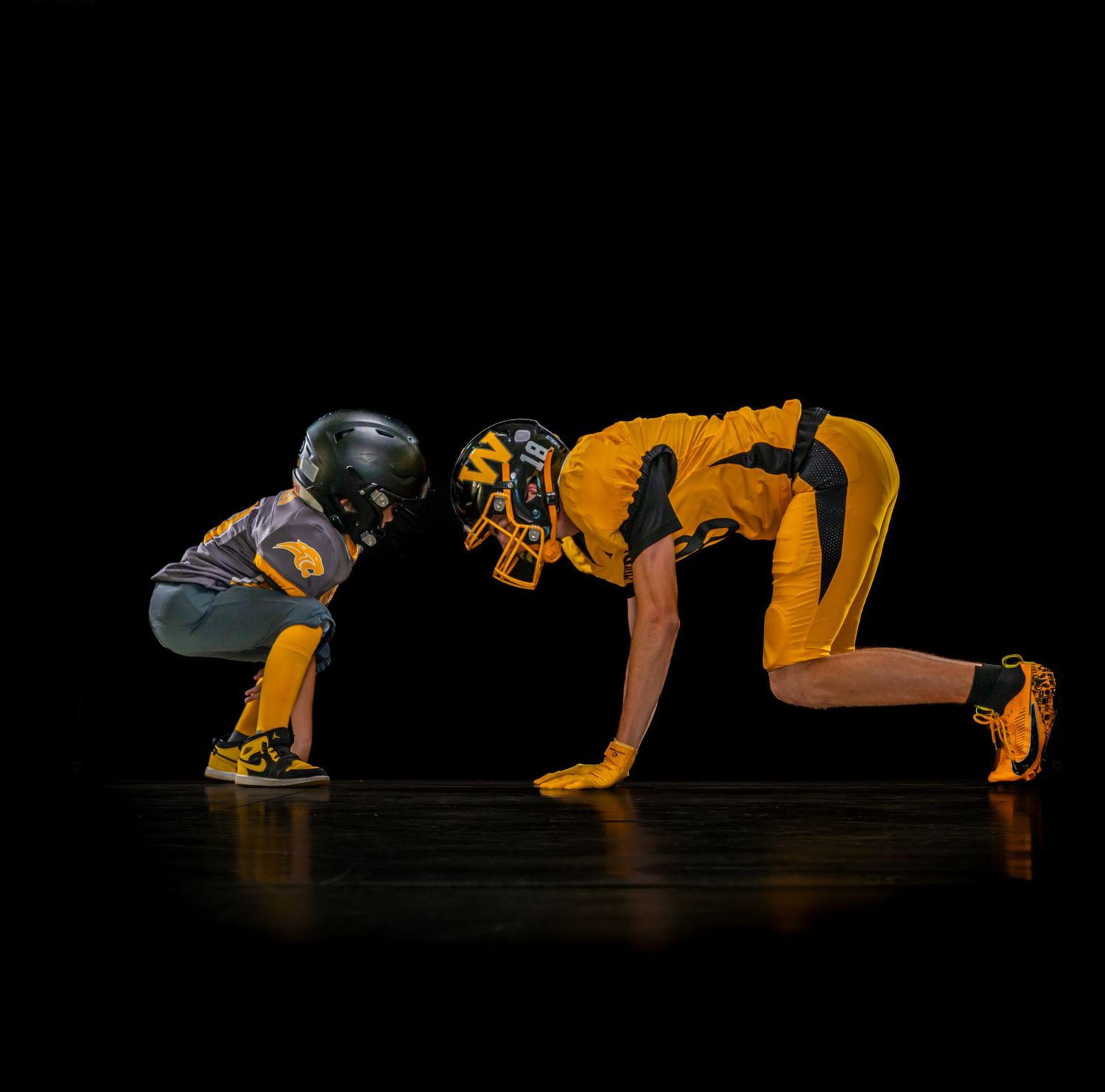 Two football players in yellow uniforms face off in a crouched stance on a dark stage.