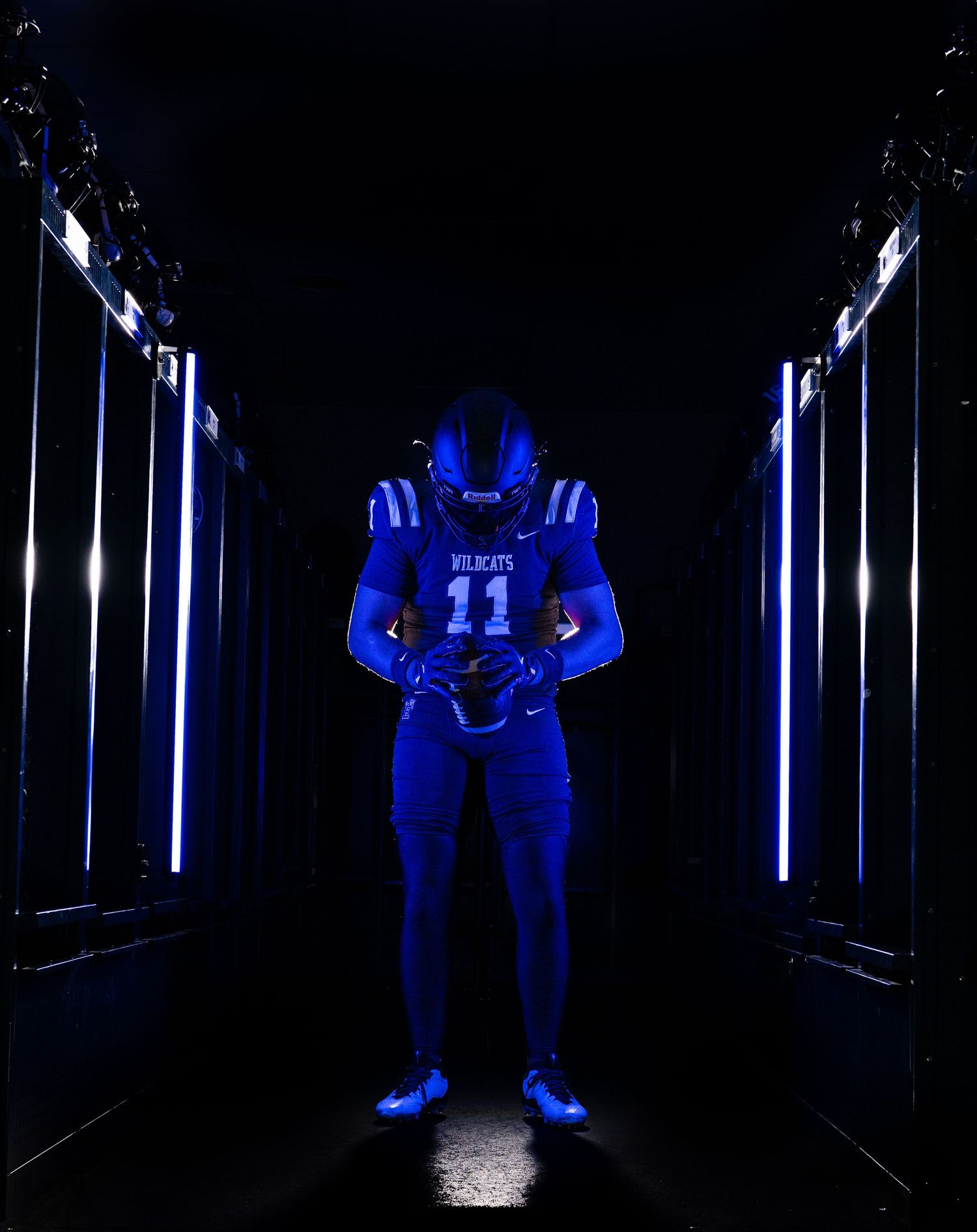 Wildcats football player #11 in blue uniform standing in dark tunnel with glowing lights.