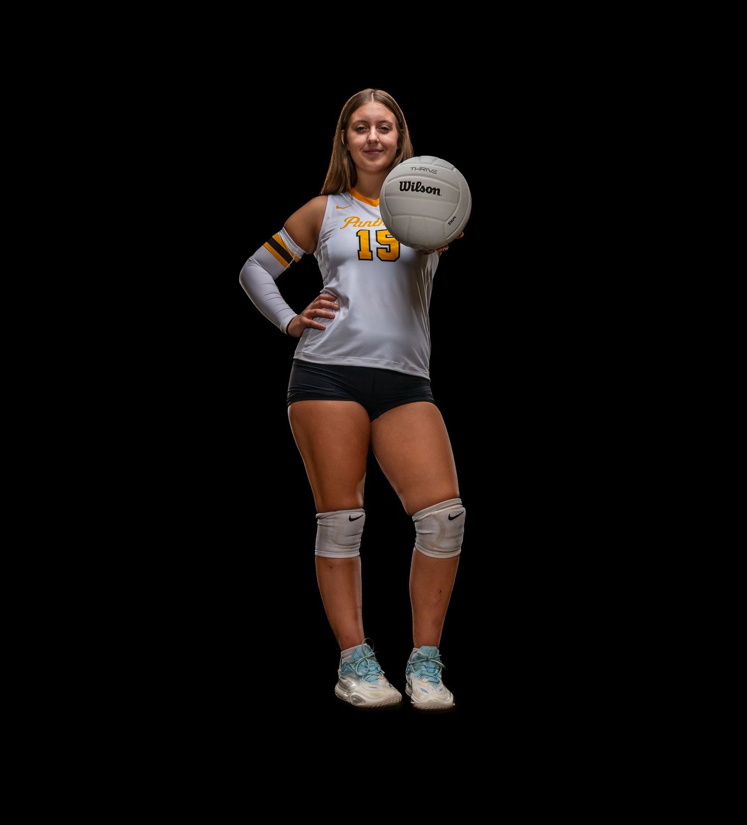 Volleyball player in athletic uniform poses with ball against dark background.
