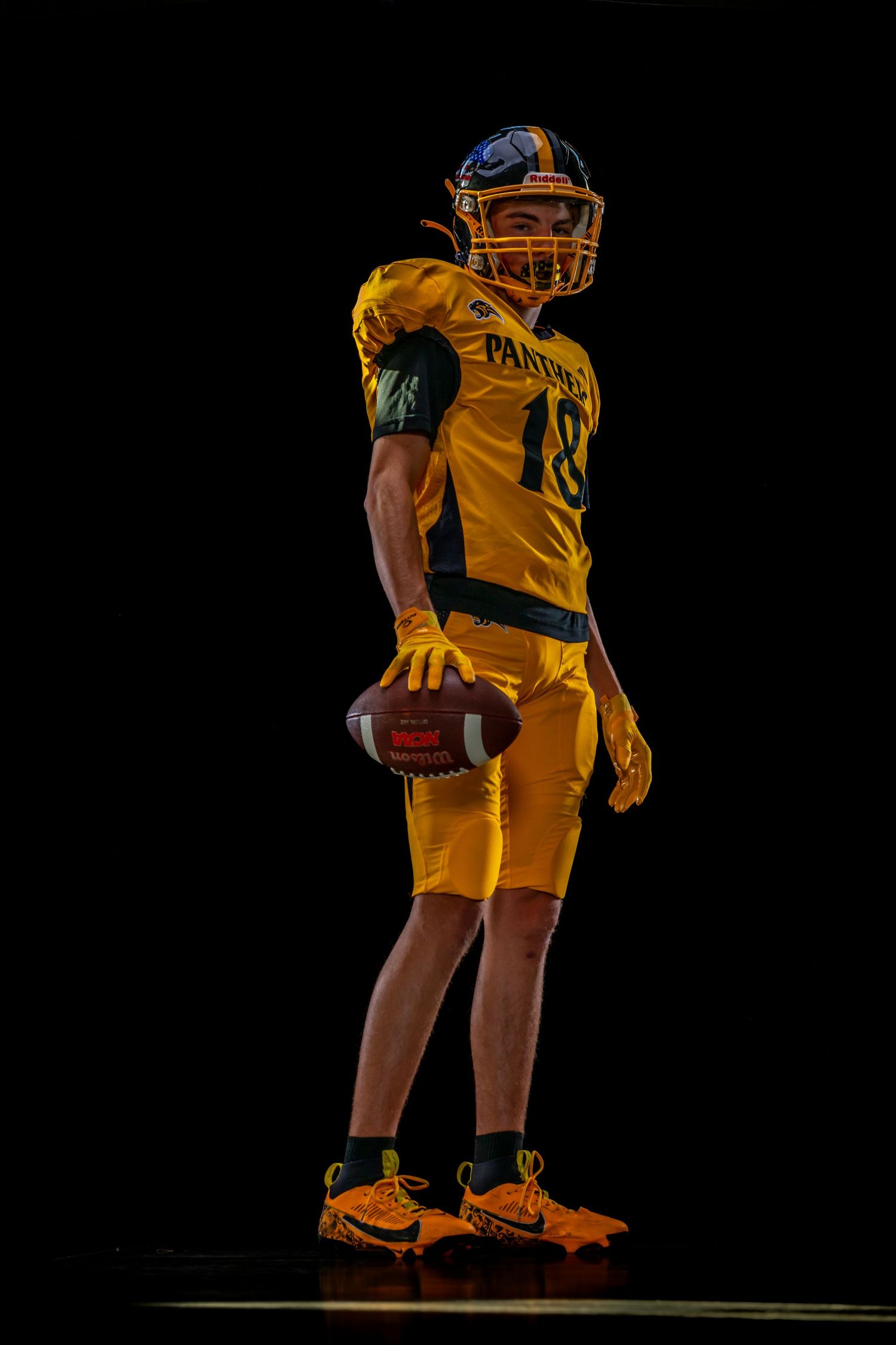 Football player in gold Panthers jersey #18 holding a football, posed against a dark background.