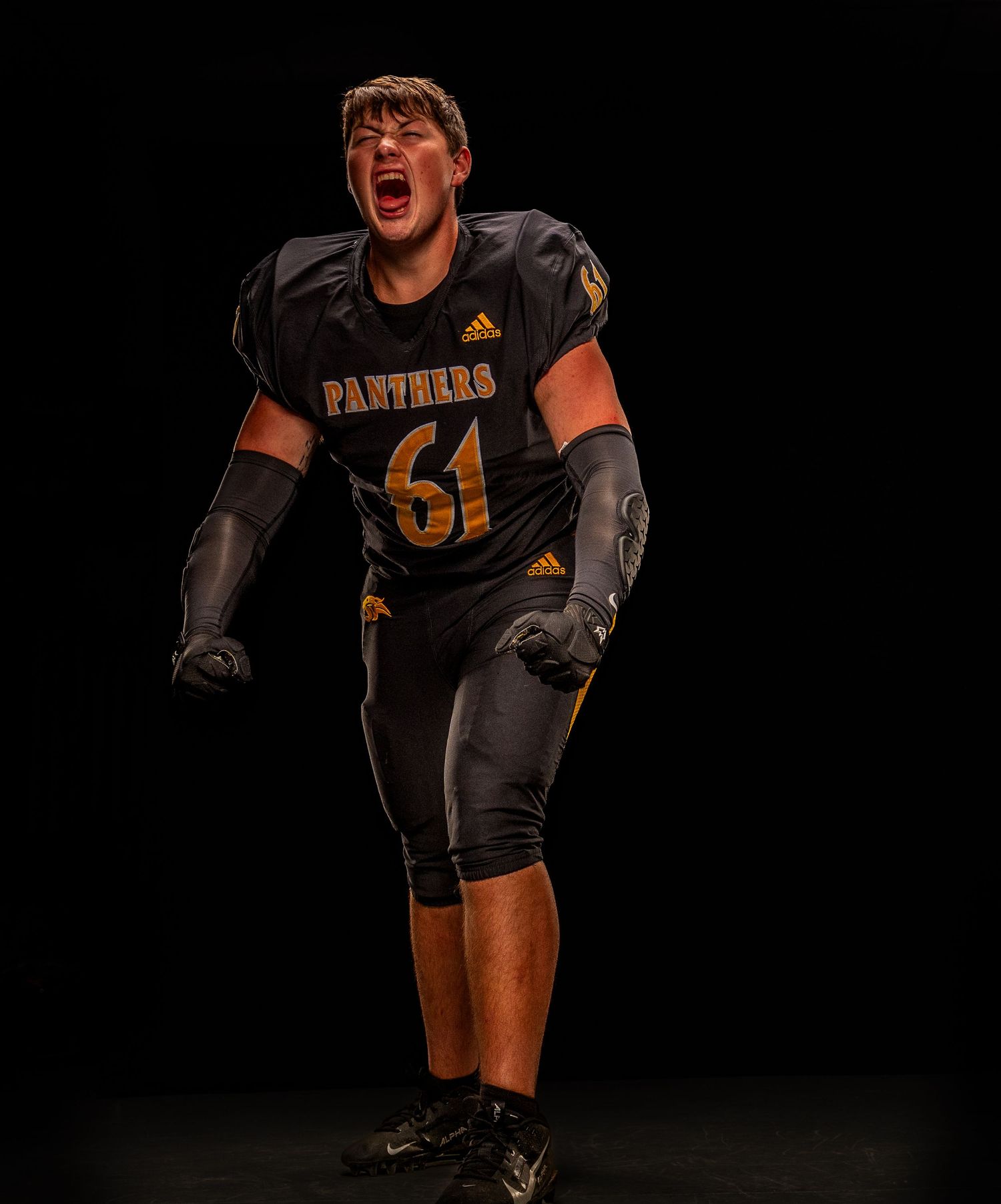 Football player wearing Panthers jersey number 61 in dark uniform, shouting with intensity against black background.