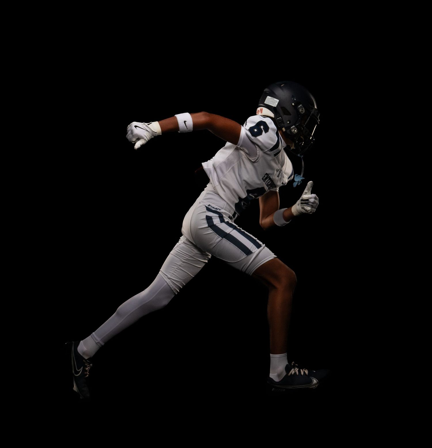 Football player in white uniform sprints in dramatic studio lighting.