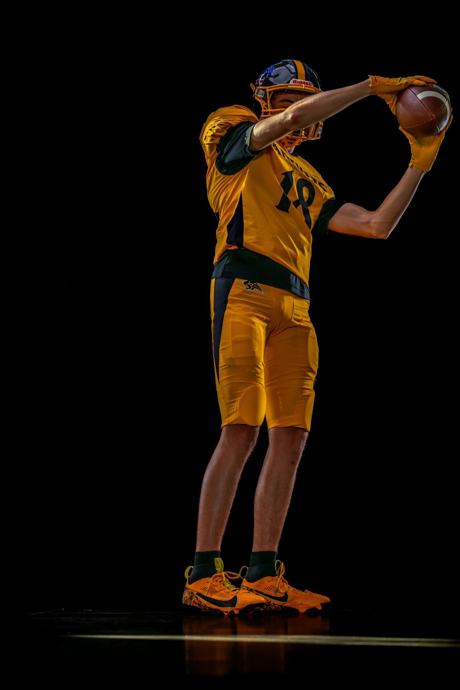 Football player in yellow uniform poised to throw a football against a dark background.
