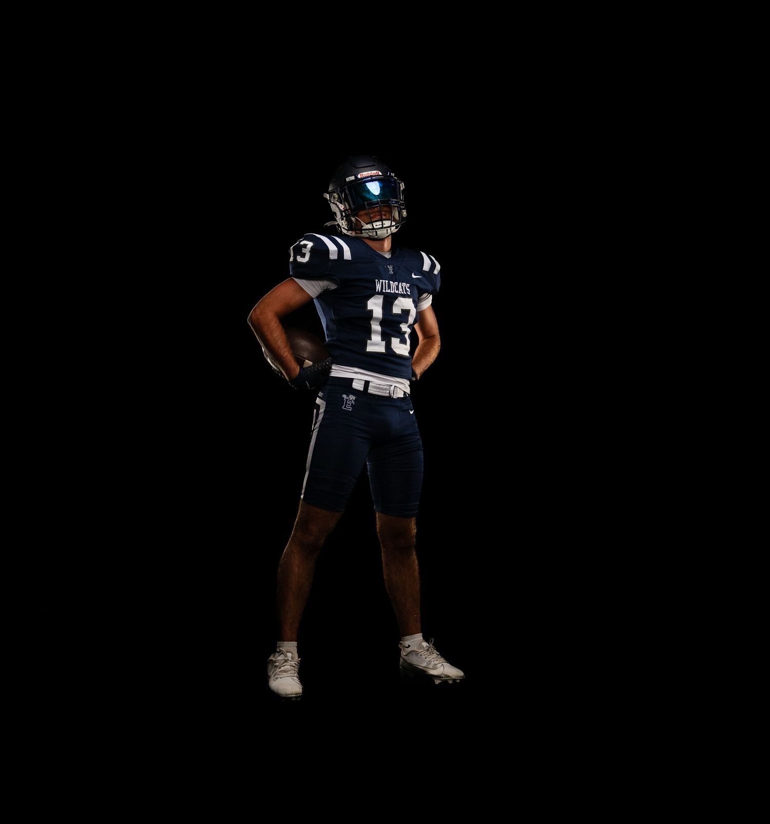 Football player wearing navy blue jersey number 13 poses confidently against a dark background.