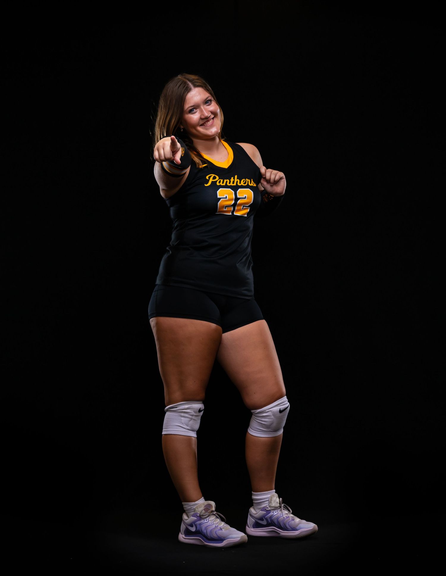 Smiling female Panthers volleyball player #22 pointing at camera in black and gold uniform.