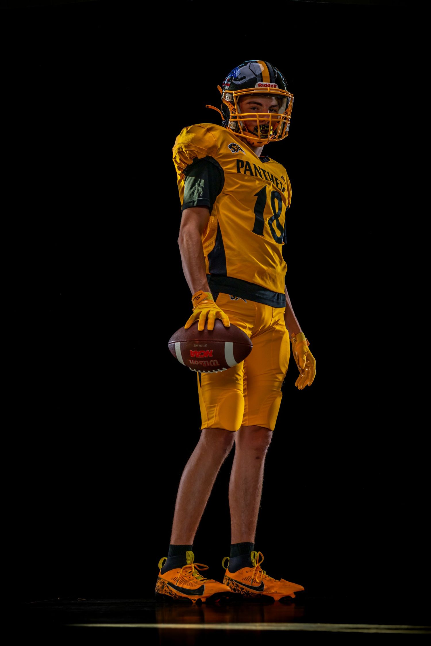 Football player in gold Panthers uniform holding a football, posed dramatically against a black background.