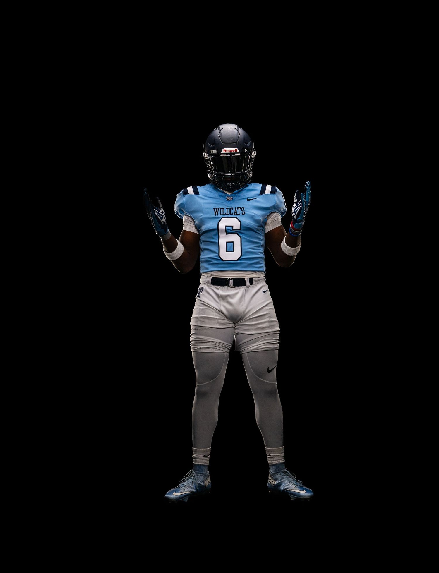Football player wearing Wildcats #6 light blue jersey and white pants uniform posed against black background.
