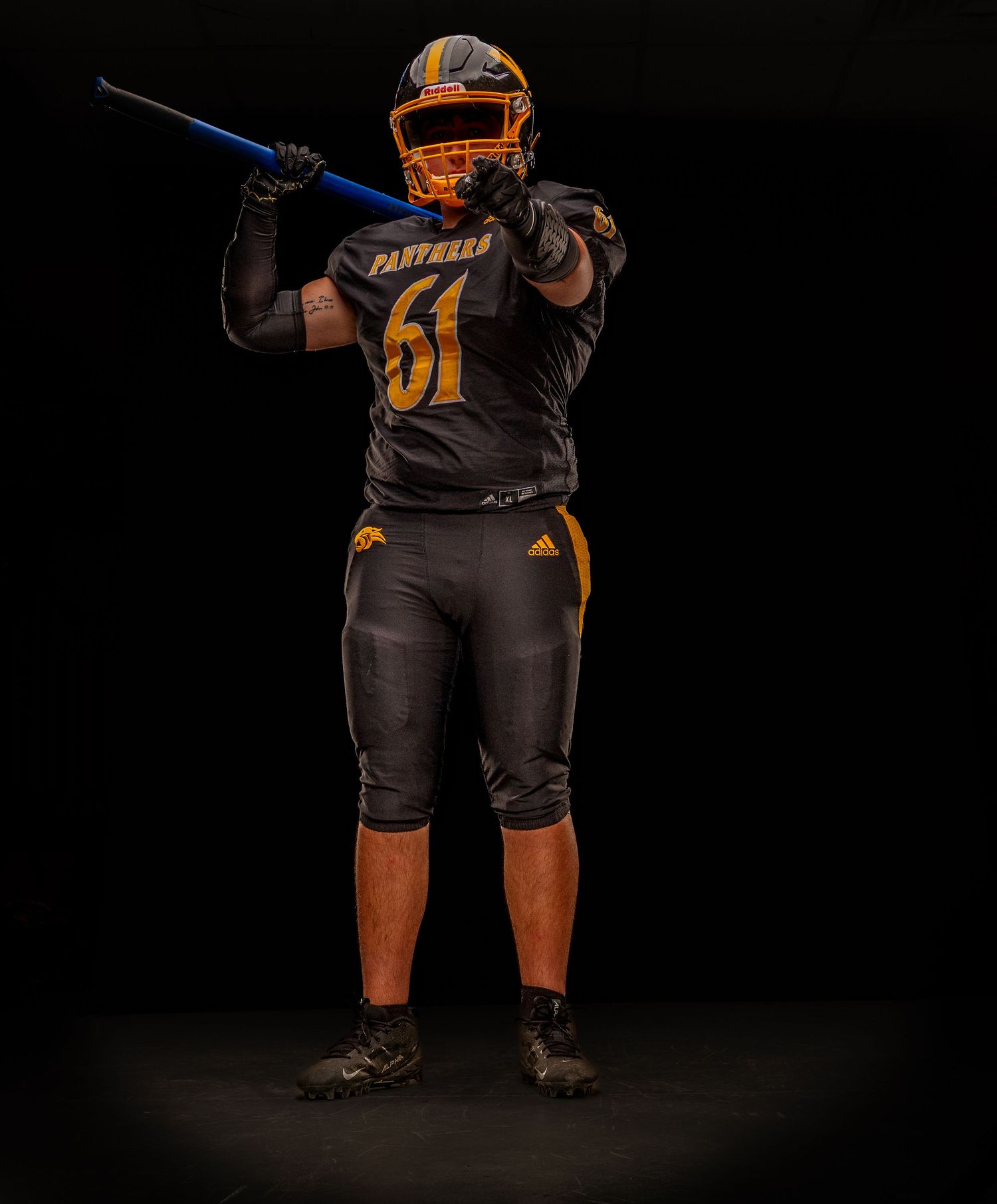 Football player in black and gold Panthers jersey number 61 holding a blue training bar in a studio setting.