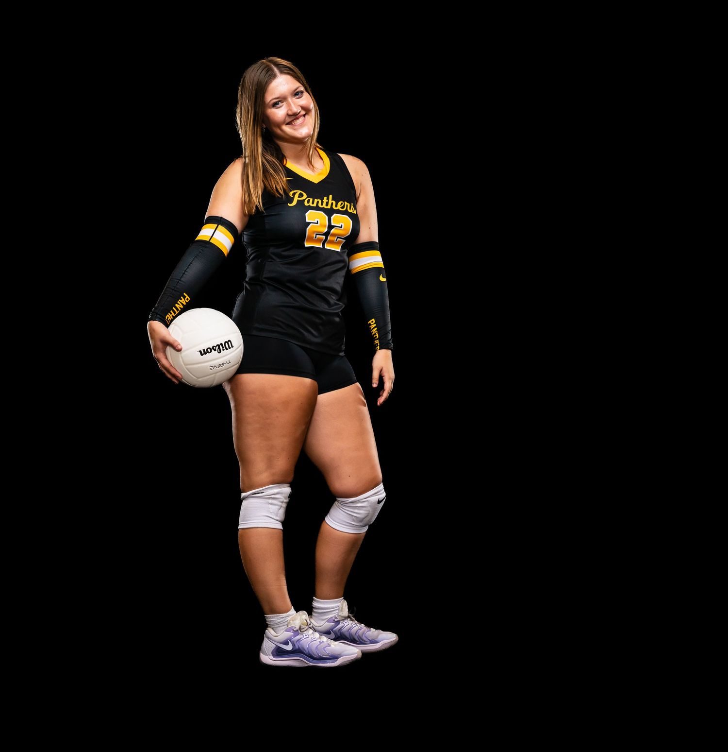 Female volleyball player in black and gold Panthers jersey number 22 holding a volleyball, wearing knee pads and purple sneakers.