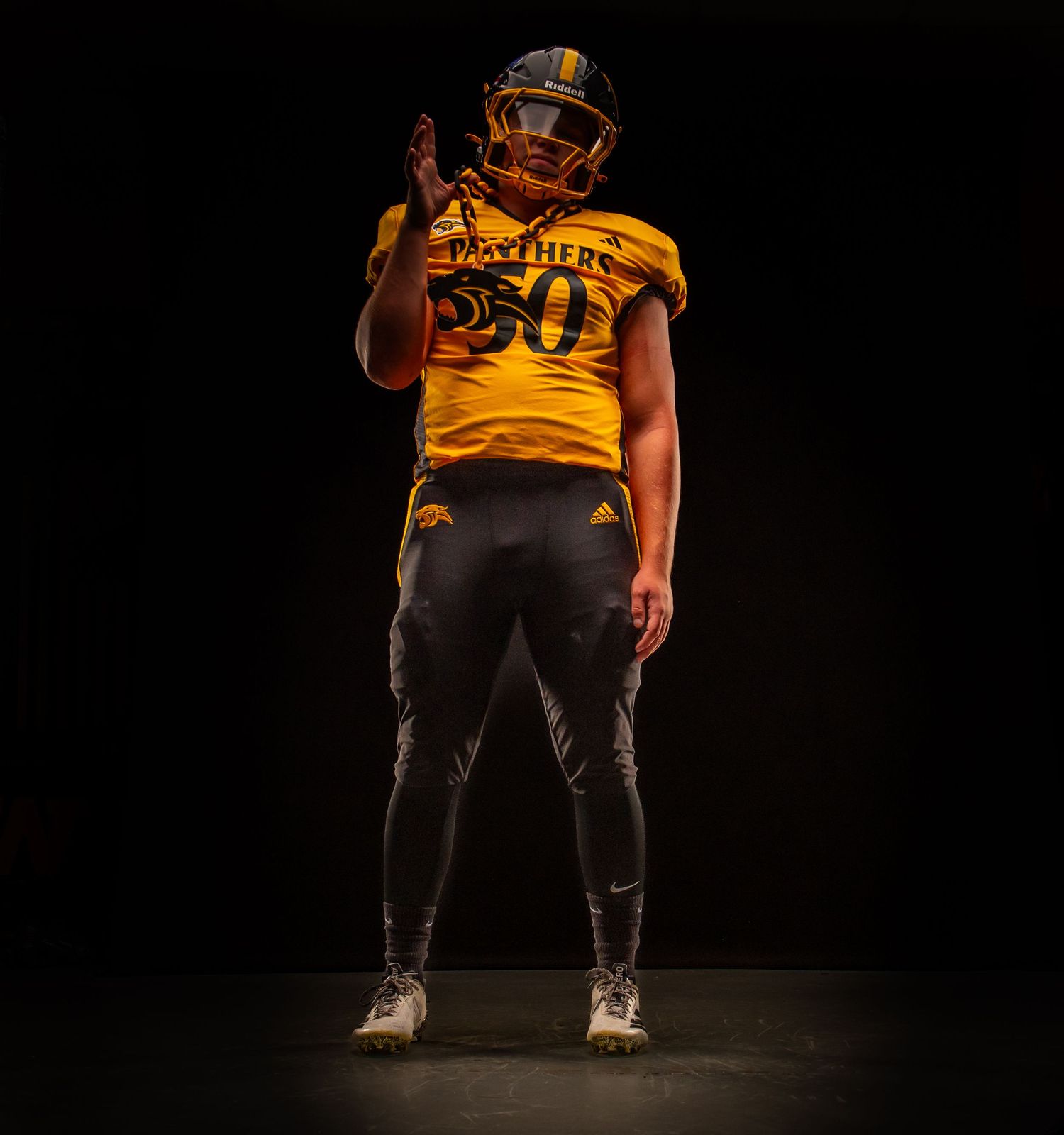 Football player wearing gold Panthers #50 jersey and black pants stands posed against dark background.