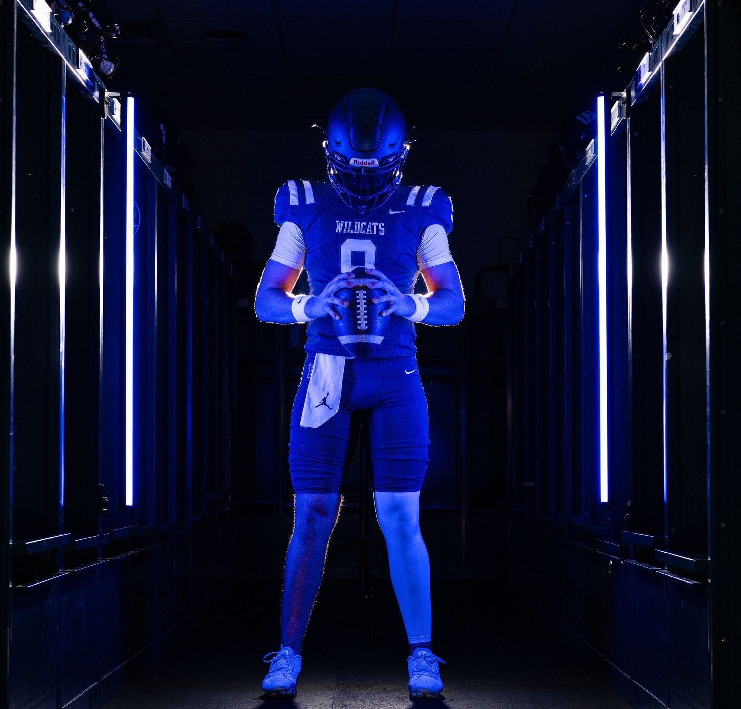 Football player in blue Wildcats uniform holding a ball, standing in a dramatic lit tunnel.