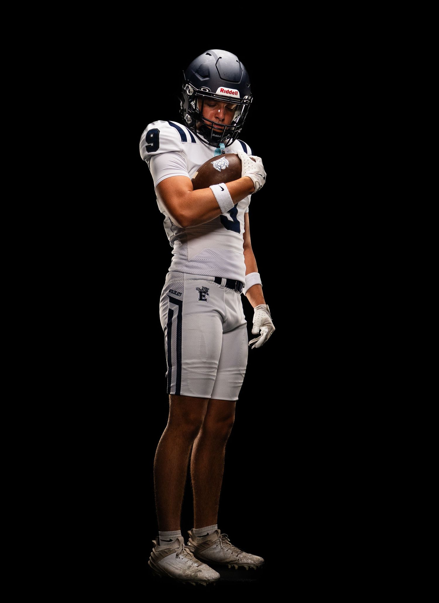 Football player in white uniform number 9 crosses arms confidently against a dark black background.