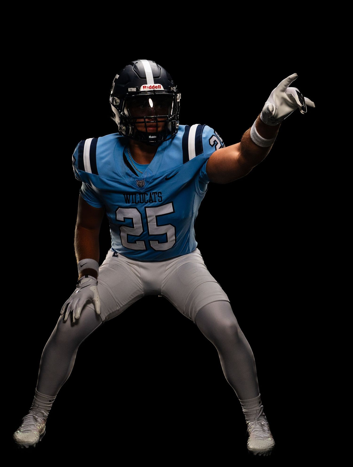 Football player number 25 in light blue uniform points finger against black background.