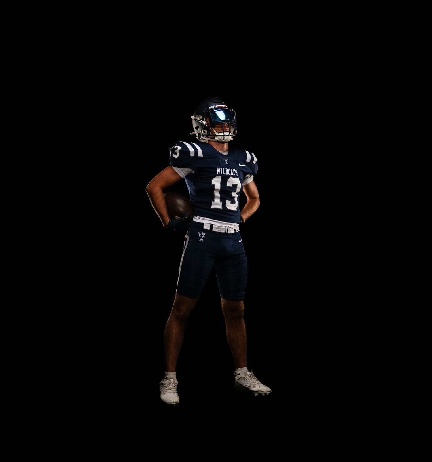 Football player in navy uniform striking athletic stance on dark background.
