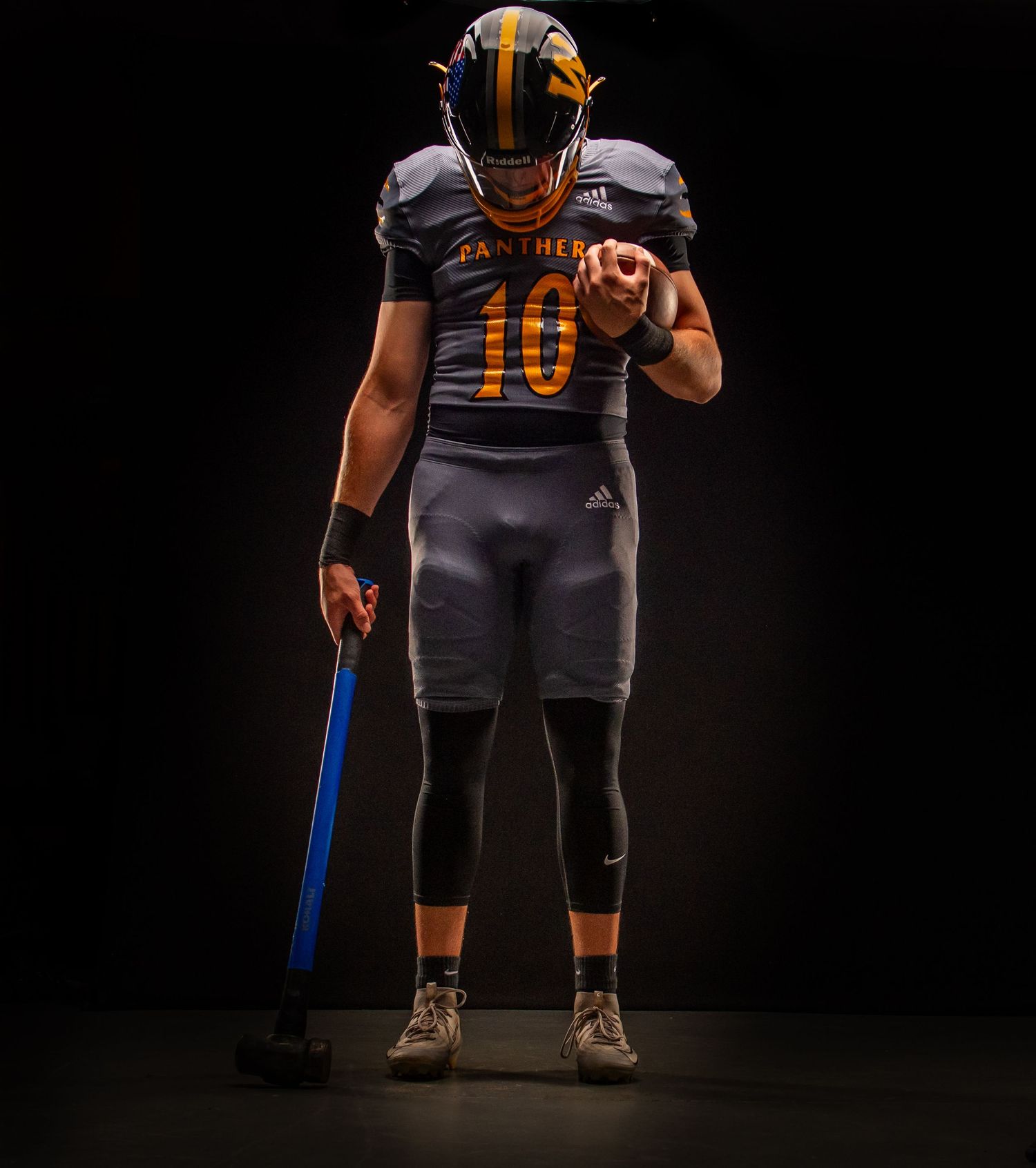 Football player wearing Panthers #10 gray and gold uniform holding a sledgehammer in dramatic dark studio lighting.