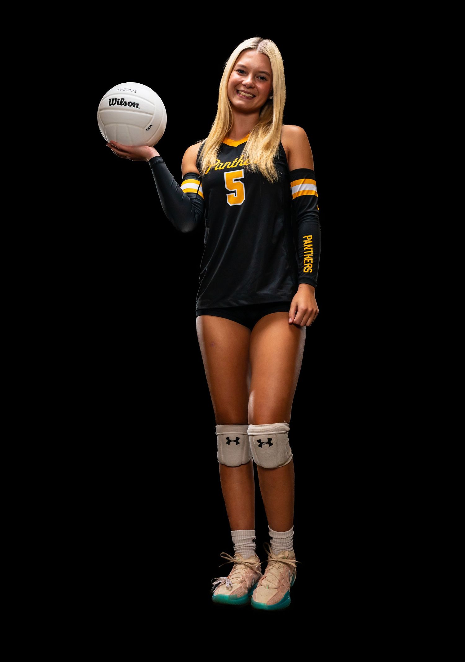 Female volleyball player in black Panthers jersey number 5 holding a Wilson ball, wearing knee pads and Under Armour gear.