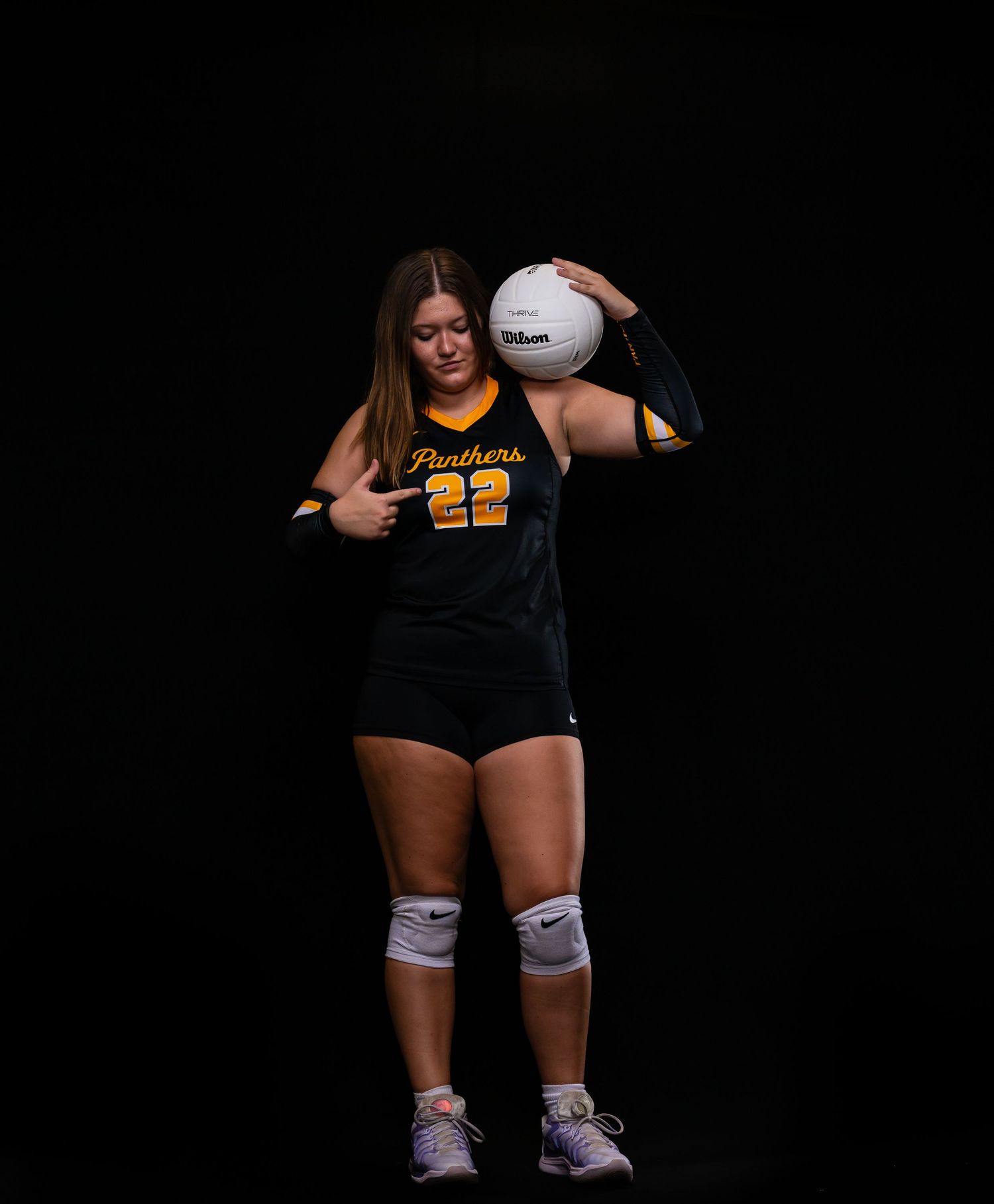 Female Panthers volleyball player #22 resting Wilson volleyball on shoulder in black uniform.