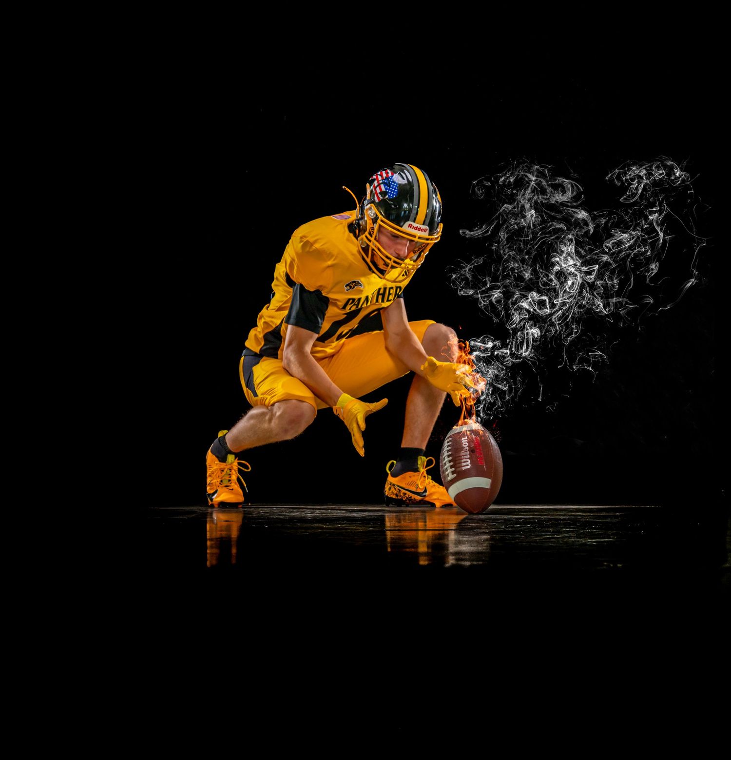Football player in gold uniform crouches with ball as smoke swirls dramatically.