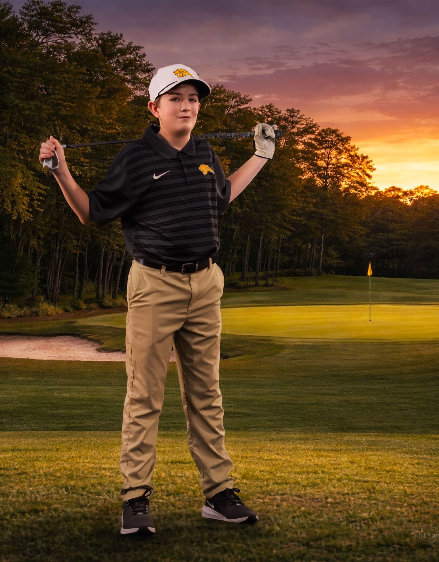 A golfer stands on a scenic golf course at sunset with dramatic orange sky and tree silhouettes in the background.