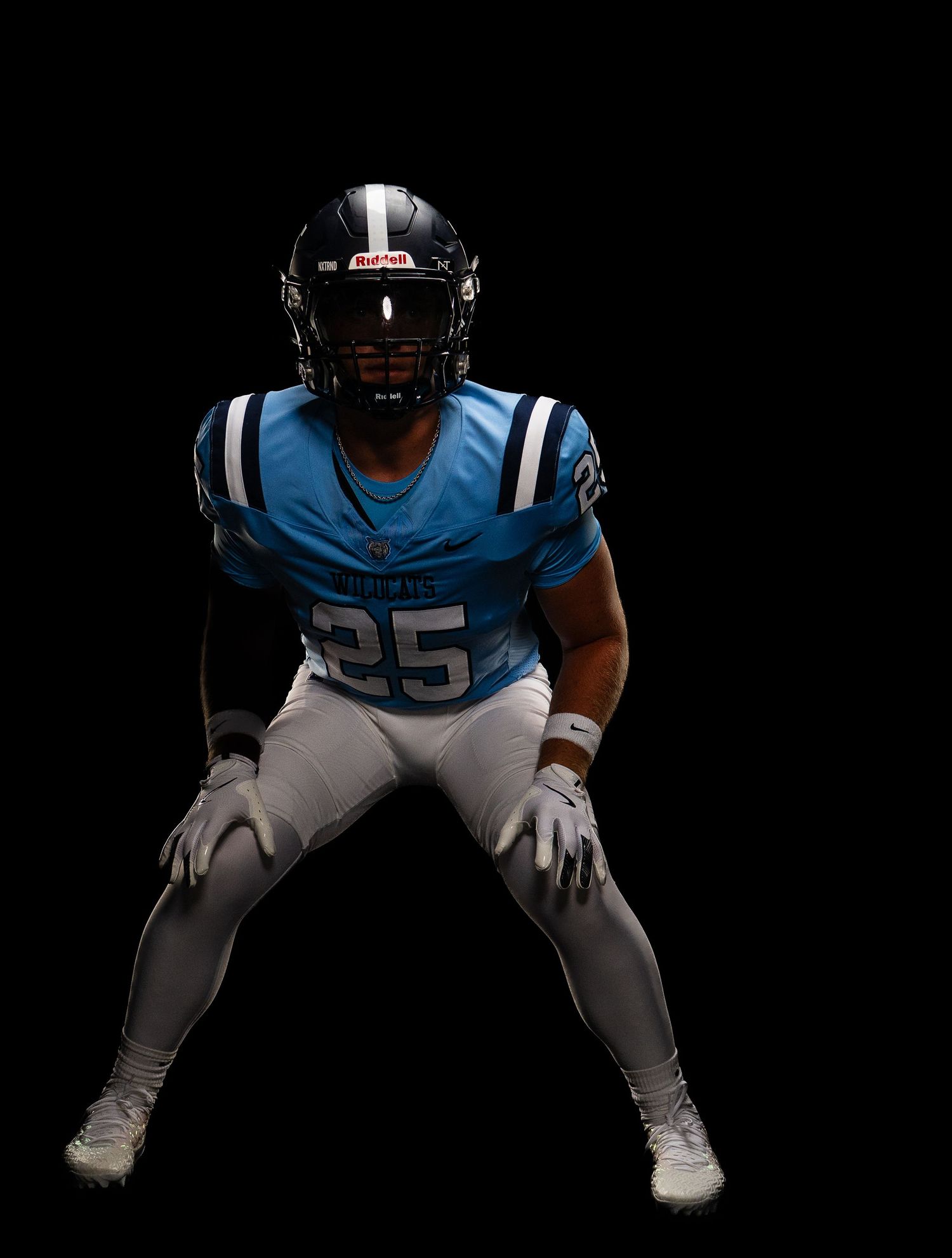 Football player wearing number 25 in blue uniform and helmet poses in athletic stance against black background.