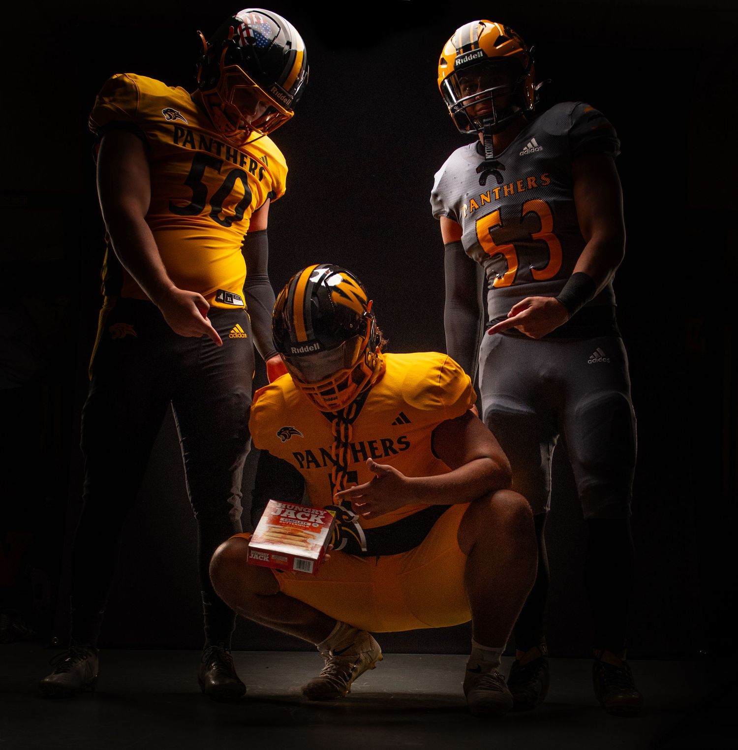Three Panthers football players in gold and gray uniforms pose dramatically under studio lighting.