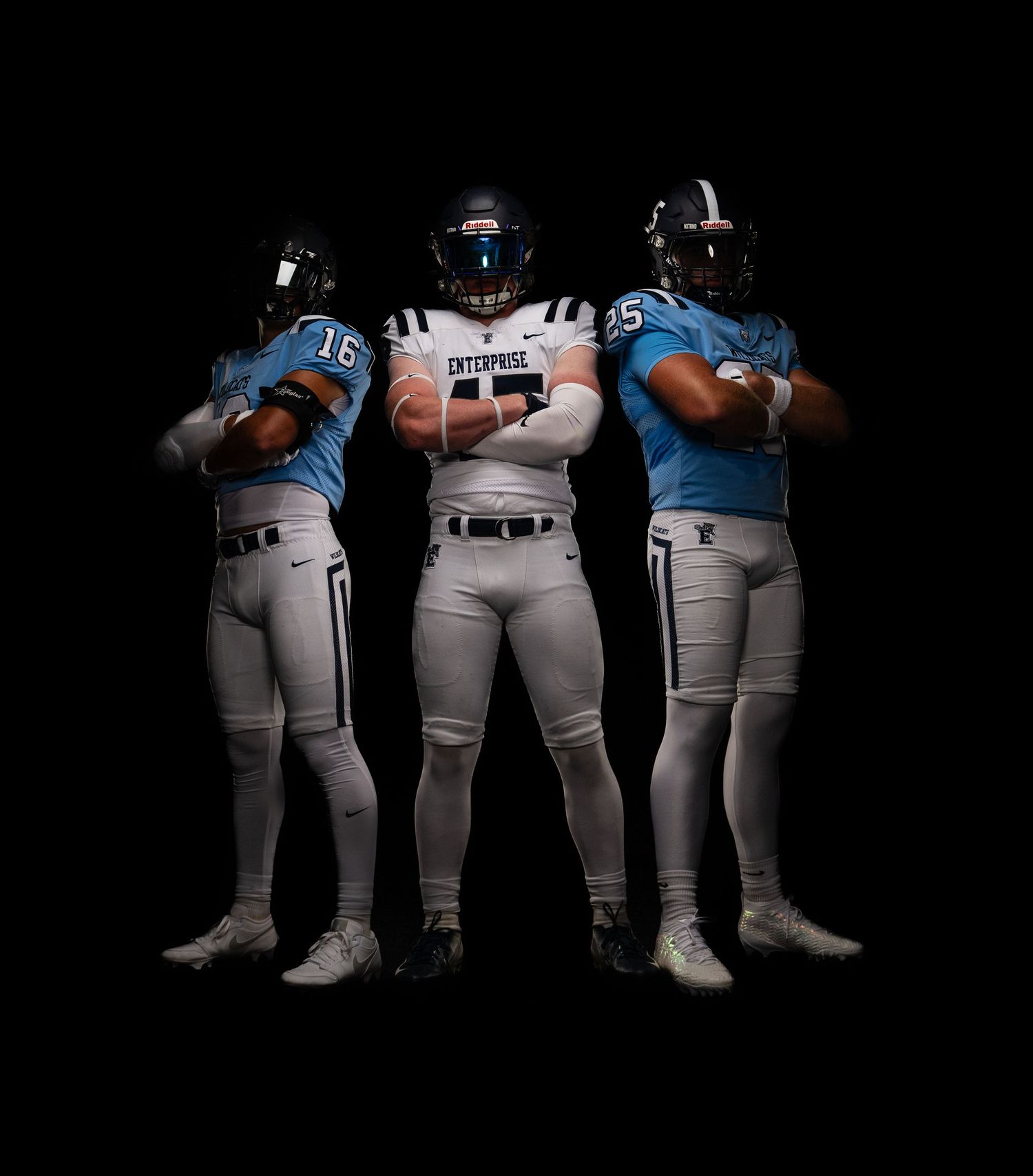 Three football players in light uniforms pose together against dark background.