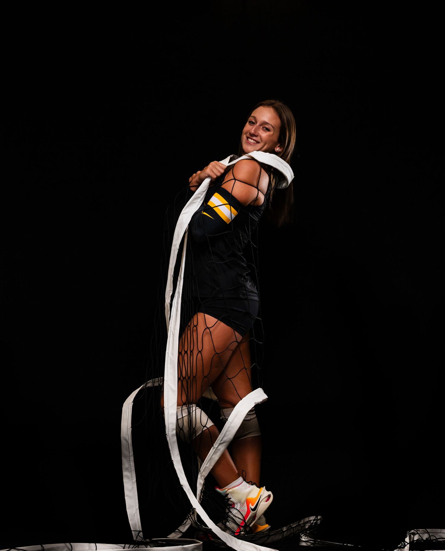 Volleyball player leaps with white streamers creating dynamic motion effect against black backdrop.