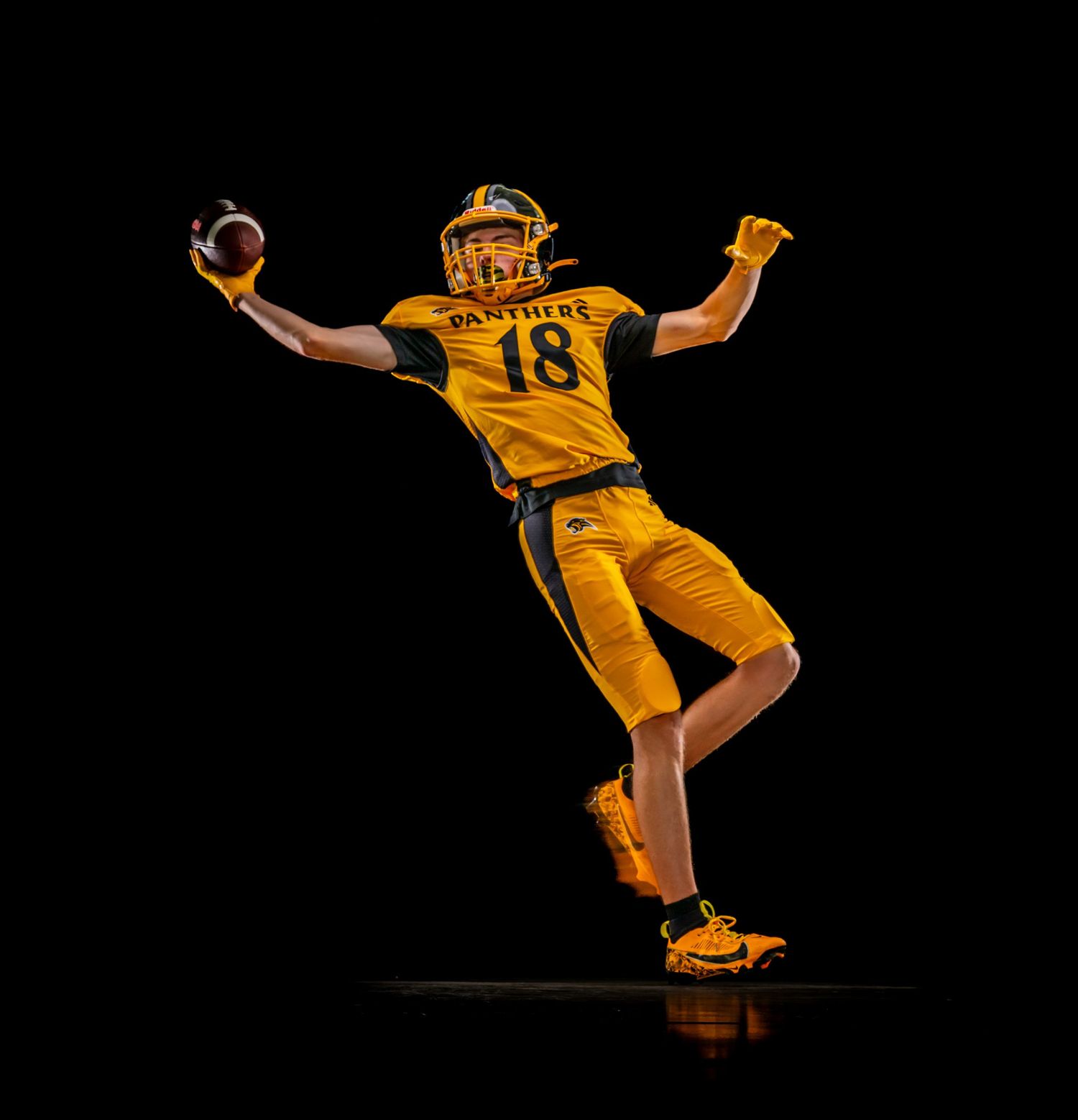Football player in yellow uniform kicking ball against dark background in dynamic action sequence.