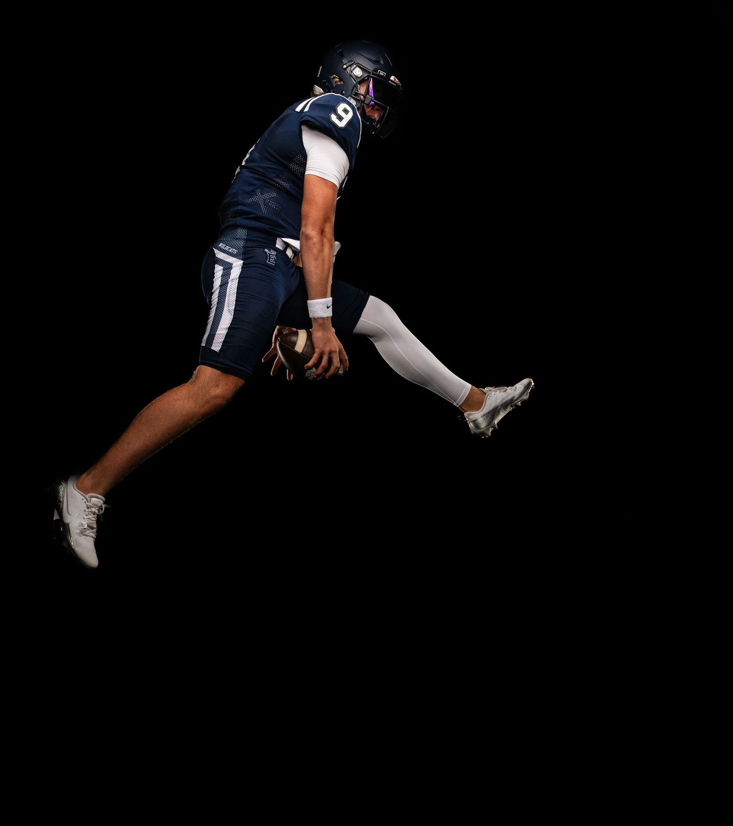 Football player in navy uniform jumping mid-air against black background.
